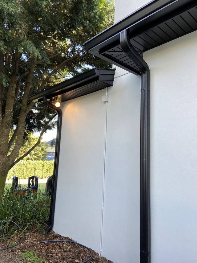 Black gutters and a ribbed downspout on a white stucco wall
