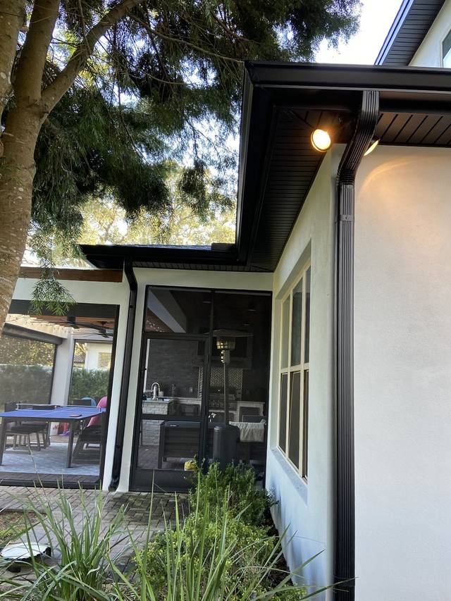 Black gutters and downspouts wrapping a corner beside a screened patio