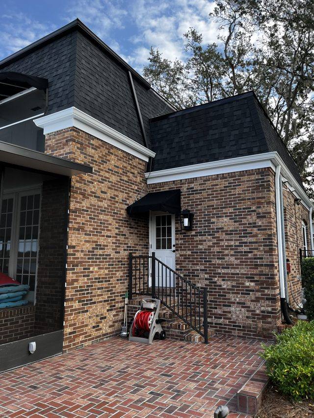White gutter and downspout at a brick corner beside a side entry