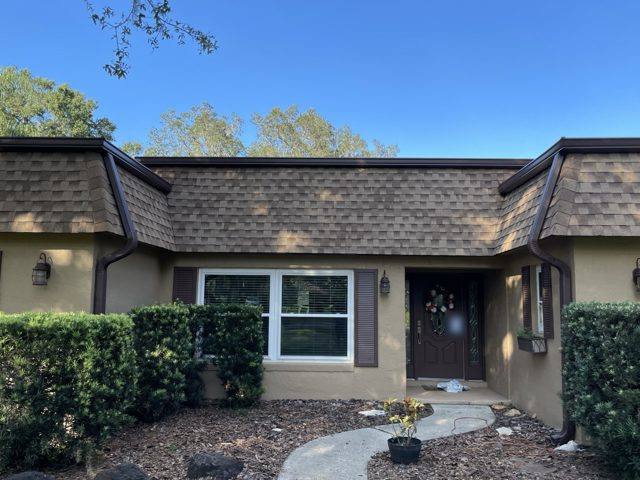 Brown gutters and downspouts on either side of the front entry of a stucco home