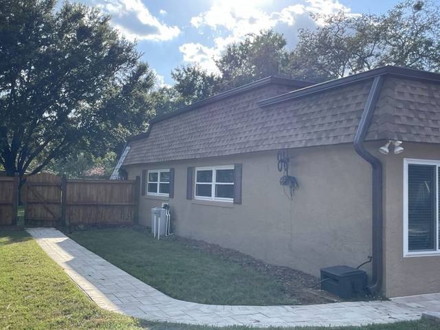 Brown gutters and a downspout on the back of a stucco home with a brown shingle mansard-style roof