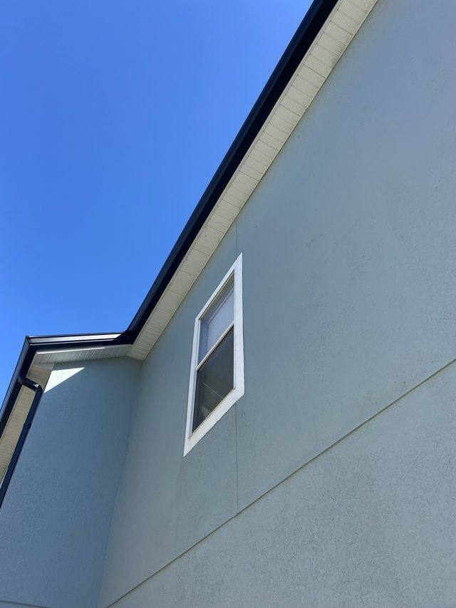 Black seamless gutter running along a roofline, with a downspout turning down at the corner