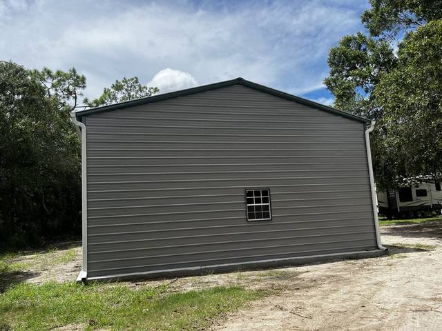 White downspouts at both corners of a gray metal building on a sandy lot