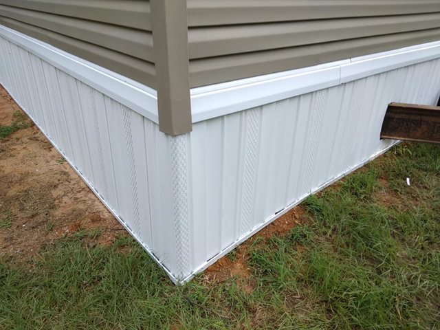 White vinyl skirting installed around the base of a mobile home, with vented panels and trim
