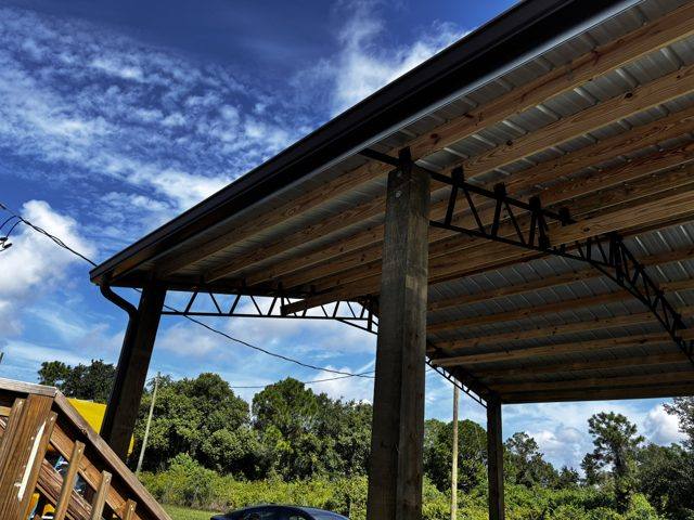 Black gutter and downspout on a pole structure with a metal roof and steel trusses