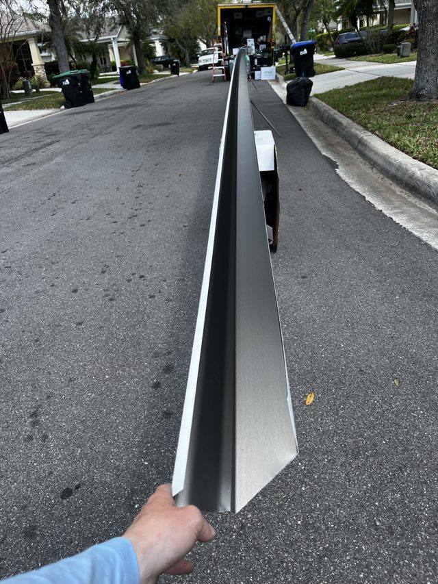 A long section of seamless gutter held up on a neighborhood street, with a truck in the background