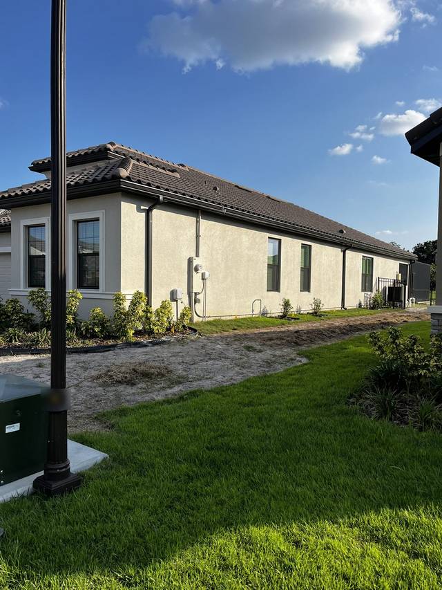 A long run of dark gutter along the side of a stucco home with a tile roof