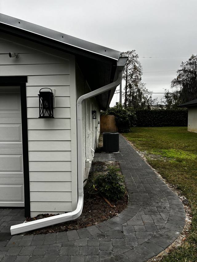 A white downspout with an angled extension ending over a paver walkway beside a garage