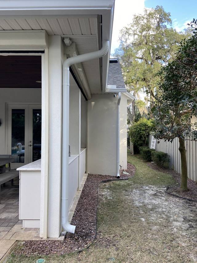 White downspouts routed around a covered patio, with outlets that direct water away from the wall