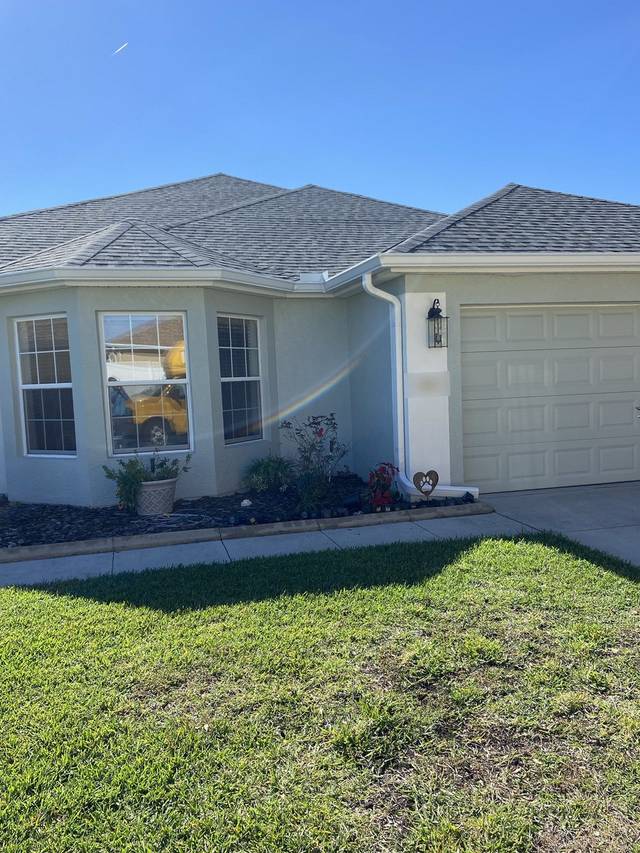 White gutter and downspout beside the garage, ending in an outlet over the flower bed