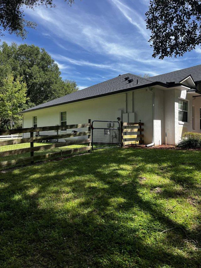 White gutters along the side of a white stucco home with a shingle roof, beside a wood fence and gate