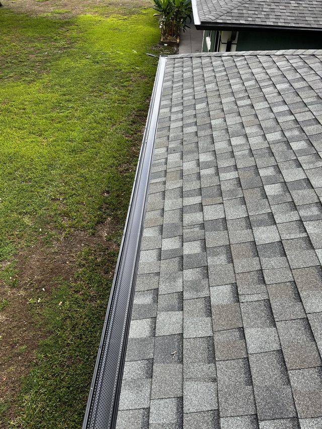 Black micro-mesh gutter guard along the edge of a shingle roof