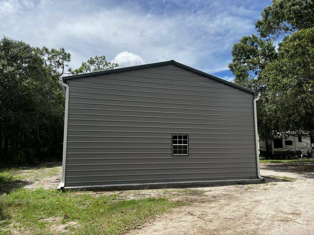 White downspouts at both corners of a gray metal building on a sandy lot
